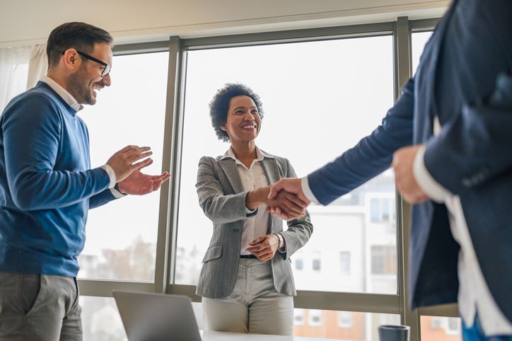 Smiling african american woman, handshaking with her colleague, while her male coworker claps.