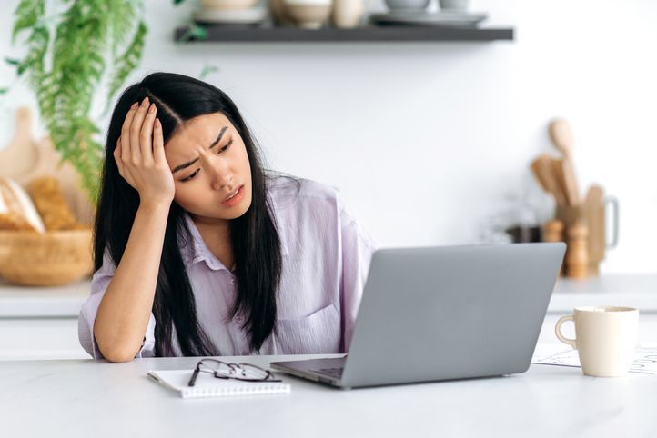 A tired woman looking at her laptop screen, head in her hand