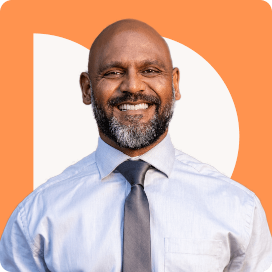 A man with a beard and a tie smiles in front of an orange background.