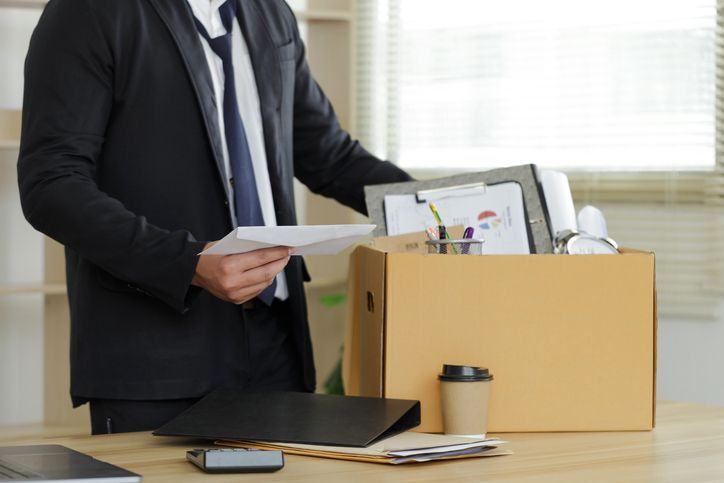 A businessman puts his box of his belongs on the desk and holds a white letter