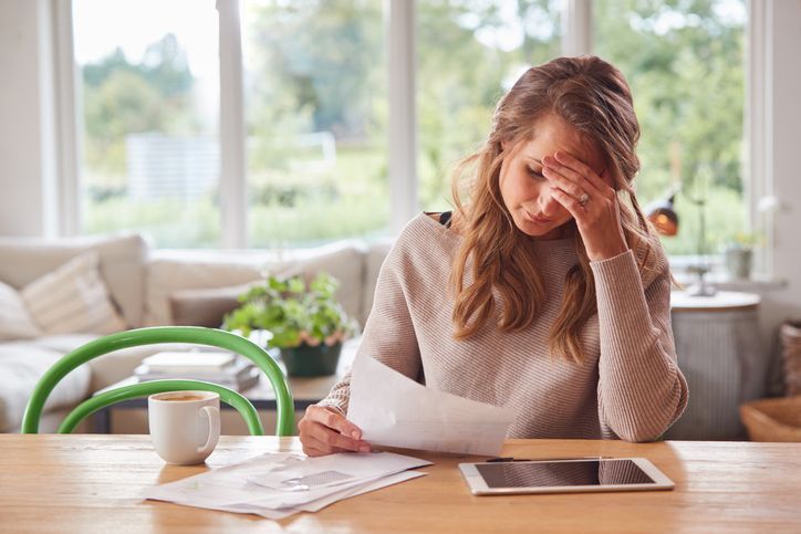 Worried Woman With Digital Tablet Sitting At Table At Home