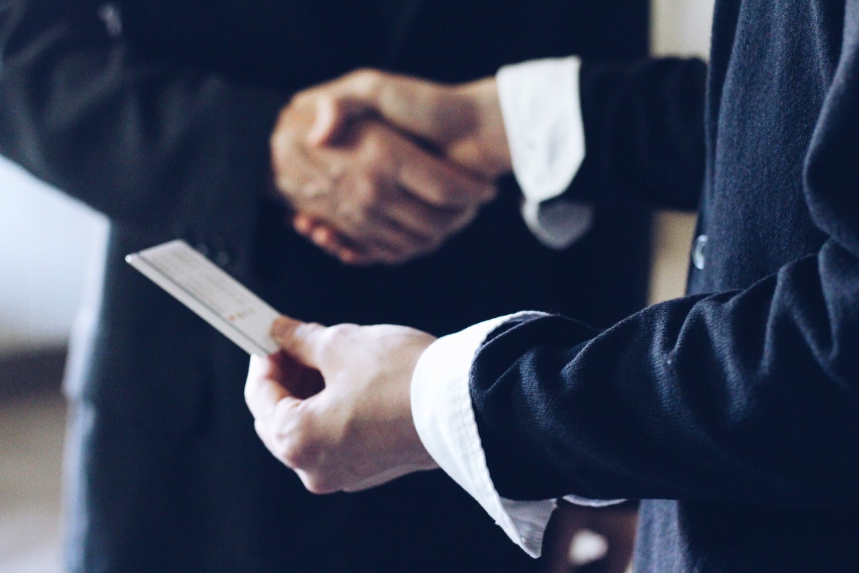 Two businessmen shaking hands while holding a credit card.