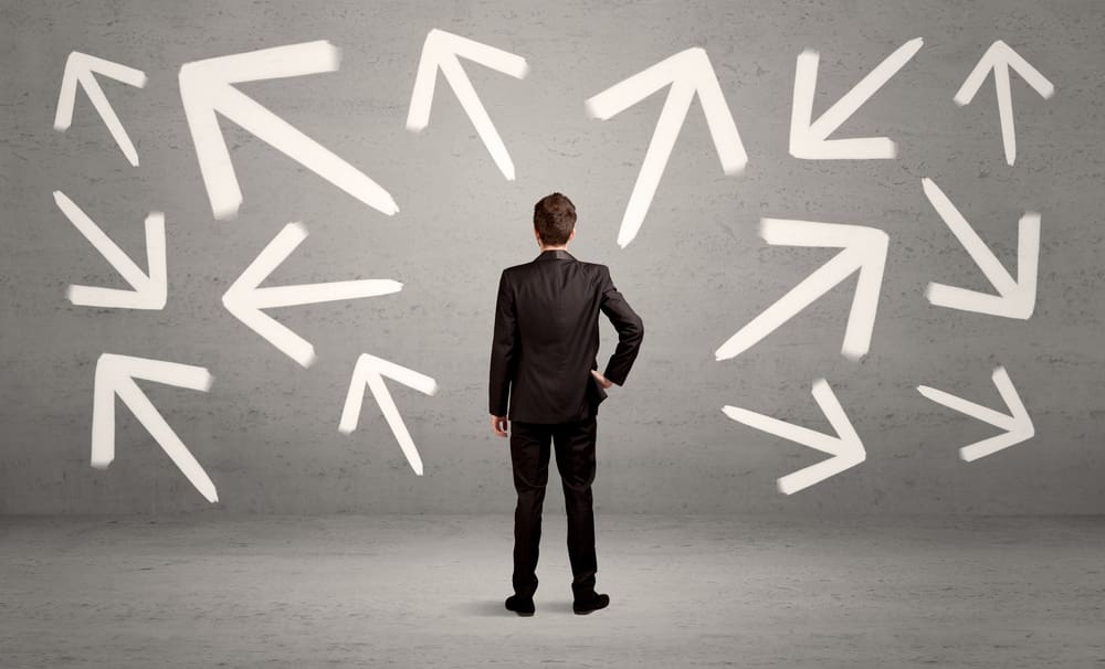 An elegant businessman standing with his back in front of urban wall full of arrows pointing in different directions