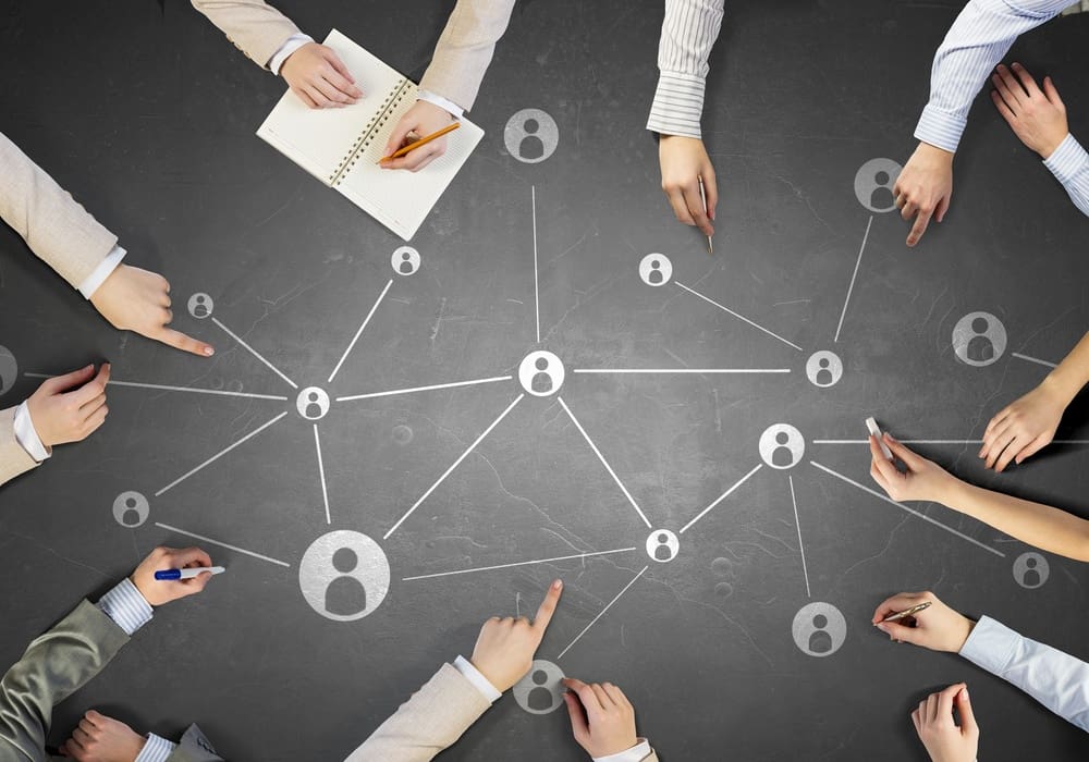 A group of business people holding hands around a network of people.