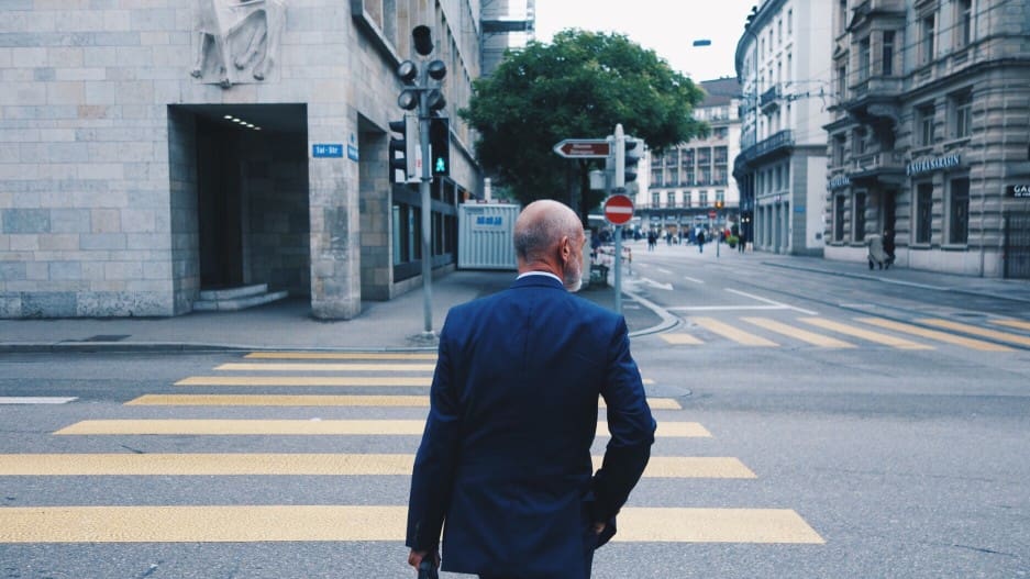 A man in a suit walking across a street.