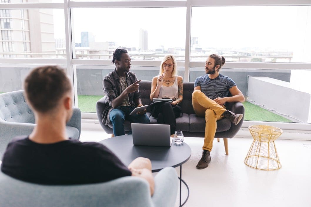 A group of people sitting around a couch in an office.