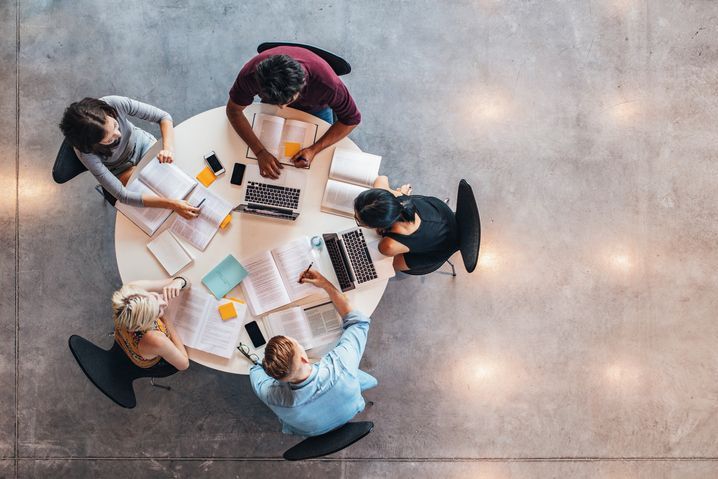 Top view of adults working at a round table, laptops and books on the table