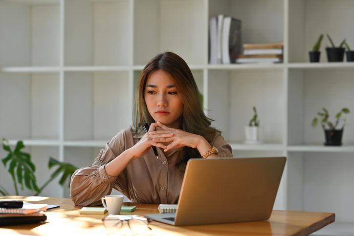 An Asian woman behind a laptop, feeling guilty