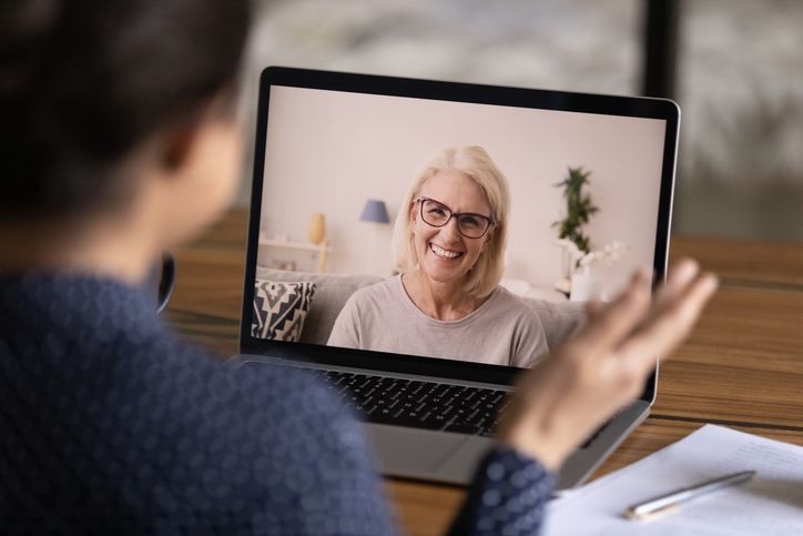 Back view of woman talking to someone virtually, on the laptop screen there is another woman