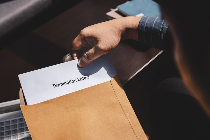 A person holds an envelope containing a termination letter, positioned over a wooden table.