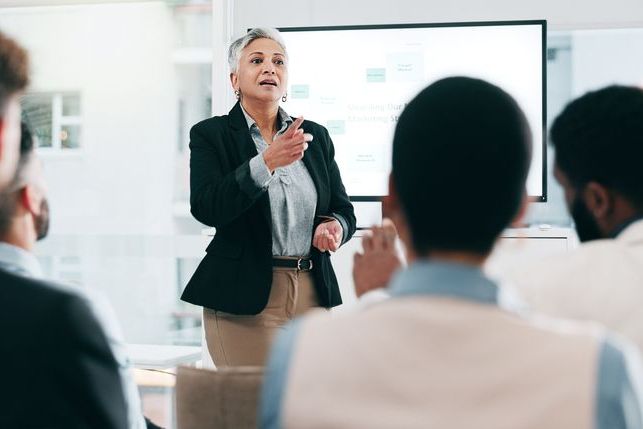 Business people, feedback and woman with presentation, seminar and questions with partnership, corporate training and discussion. Presenter, speaker and audience in a workshop, learning and crowd