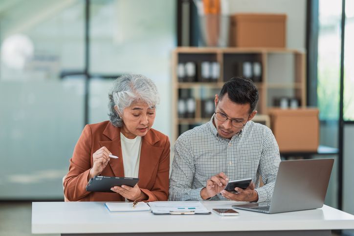 Senior Asian business woman and young man working together analyzing finances senior staff teach marketing and planning to younger staff woman holding graph and chart with a happy smile