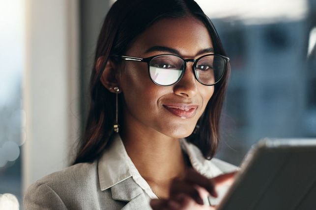 Tablet, overtime and happy woman in office with glasses, reflection with planning and website. Vision, smile and businesswoman typing email, late at night work and research on future ideas for agency