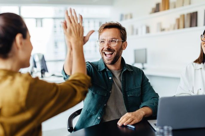 Successful business people giving each other a high five in a meeting. Two young business professionals celebrating teamwork in an office.