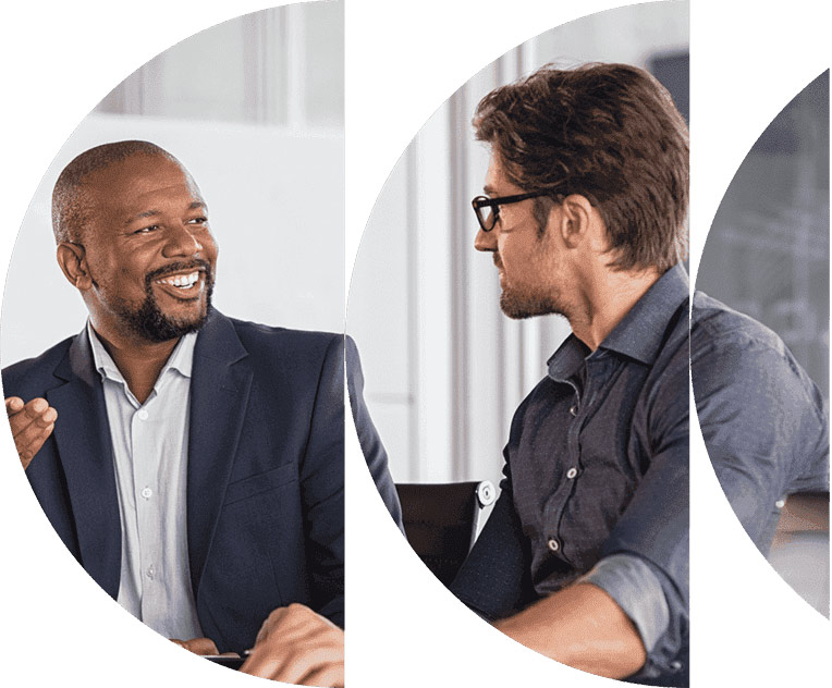 Two men, one in a navy suit and the other in a gray shirt, engage in a friendly conversation in a professional setting.