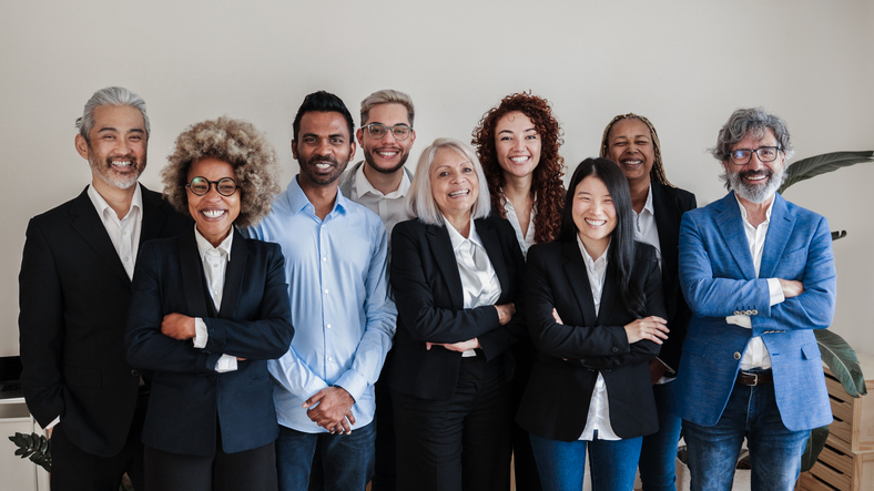 A diverse group of nine people in professional attire stands smiling with crossed arms.