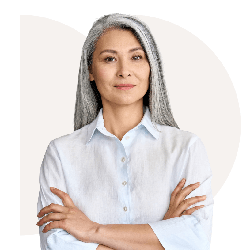 A woman with long gray hair and a white button-up shirt stands with her arms crossed, looking confidently ahead.