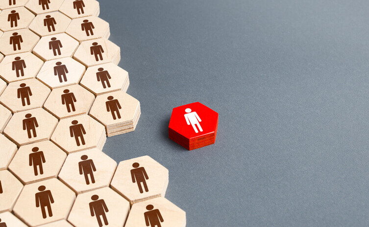 Wooden hexagonal tiles with human icons grouped together, except for one red hexagon with a white human icon placed apart from the group, symbolizing exclusion or separation.
